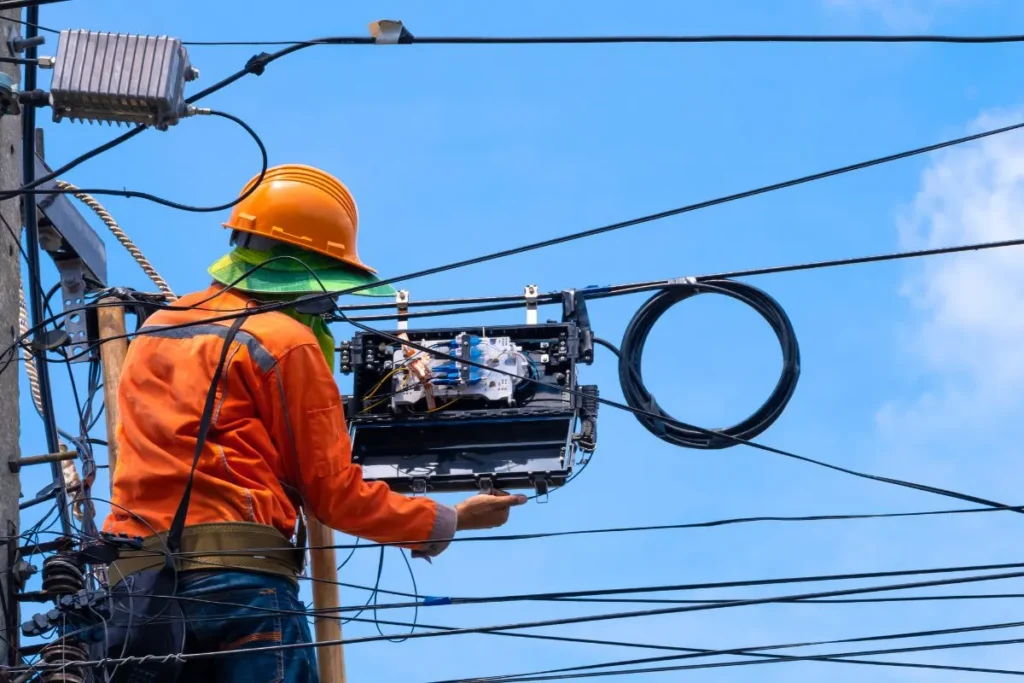 Technicien EDS Cabling en combinaison orange installant un boîtier de câblage sur un poteau électrique en Belgique